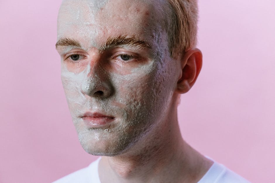 Portrait of a young man with a clay face mask against a pink background, highlighting skincare and beauty routines