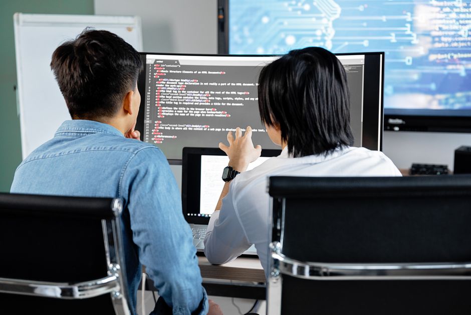 Two developers working together in an office, discussing code on a screen.